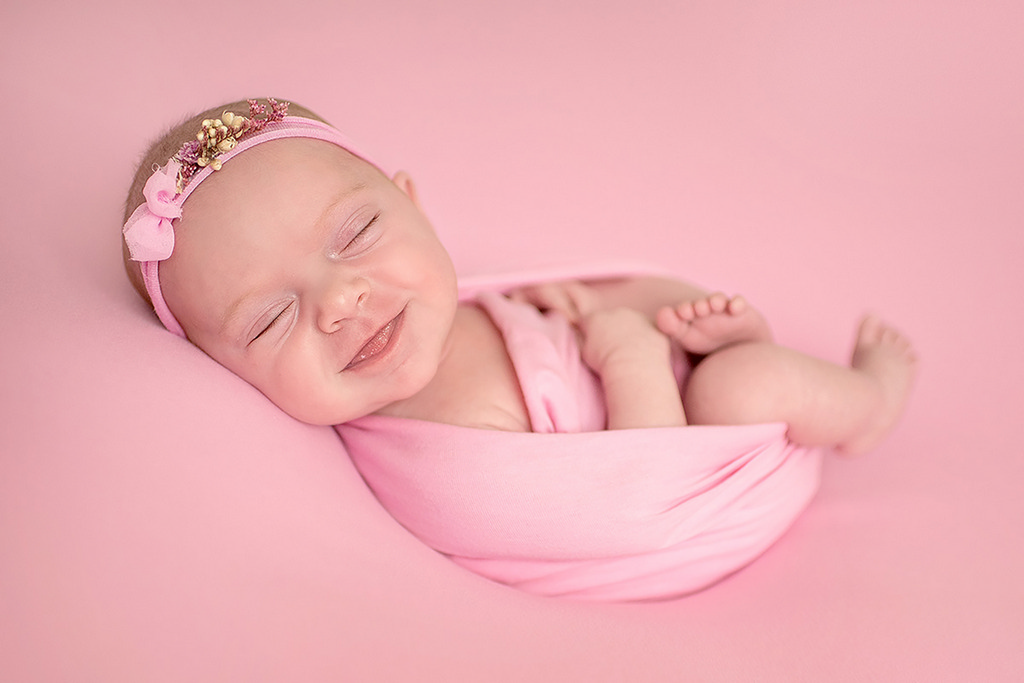 little girl newborn with tongue sticking out as she smiles sleeping