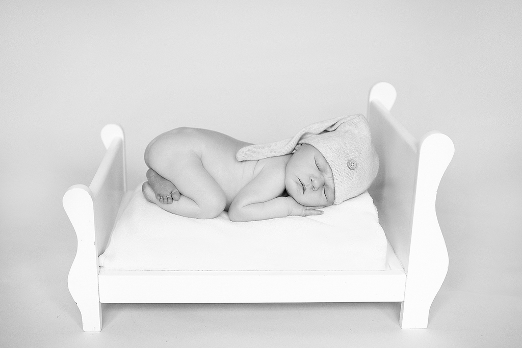 newborn baby asleep in a small bed with a cute sleeping hat on