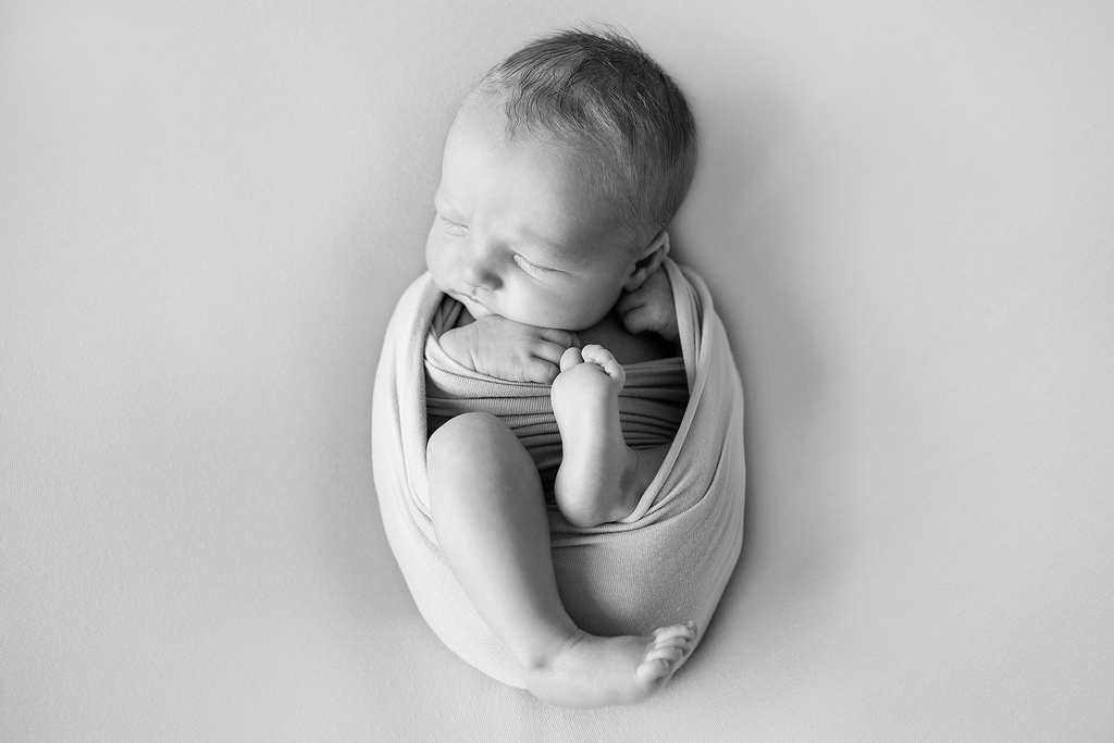 newborn baby wrapped up tightly in black and white setting